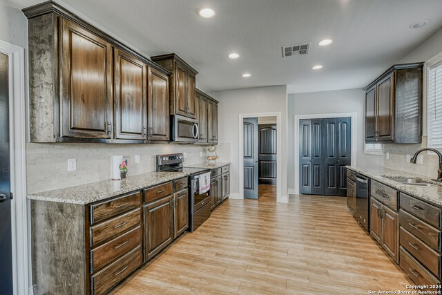 kitchen with light stone countertops, sink, light wood-type flooring, stainless steel appliances, and dark brown cabinetry