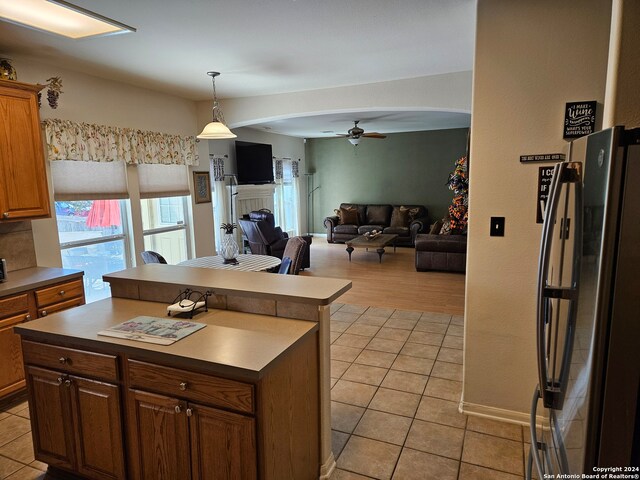 kitchen featuring hanging light fixtures, ceiling fan, a kitchen island, stainless steel refrigerator, and light hardwood / wood-style flooring