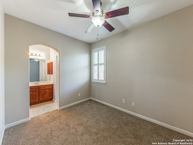 unfurnished bedroom featuring connected bathroom, sink, light carpet, and ceiling fan