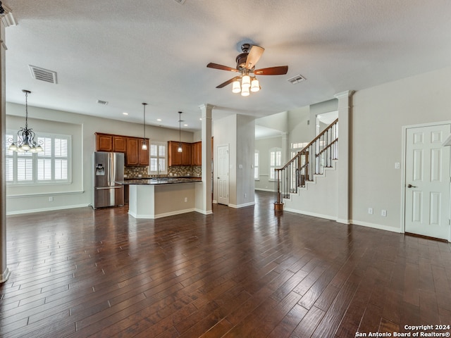 unfurnished living room with dark hardwood / wood-style flooring, ceiling fan with notable chandelier, and ornate columns