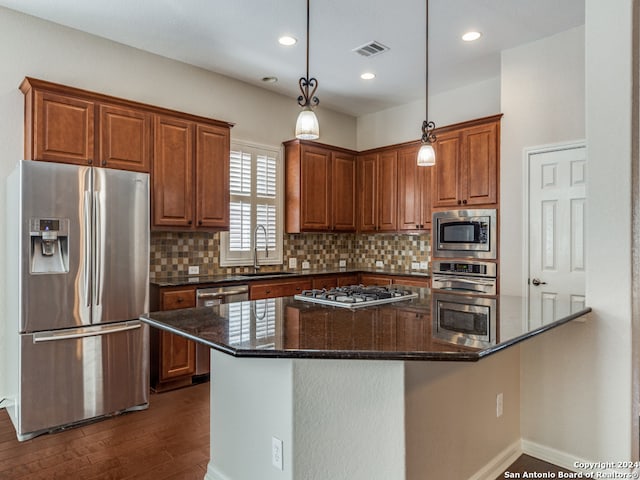 kitchen featuring sink, appliances with stainless steel finishes, pendant lighting, dark stone counters, and decorative backsplash