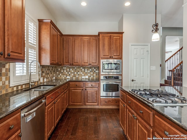 kitchen featuring dark wood-type flooring, sink, dark stone countertops, appliances with stainless steel finishes, and pendant lighting