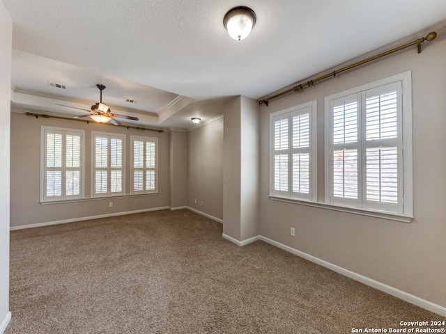 carpeted empty room featuring ornamental molding, ceiling fan, and a tray ceiling