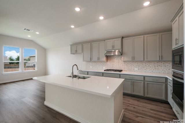 kitchen featuring lofted ceiling, a center island with sink, appliances with stainless steel finishes, gray cabinetry, and sink