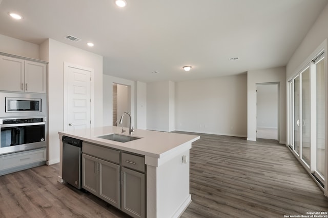 kitchen with a kitchen island with sink, dark hardwood / wood-style floors, gray cabinetry, sink, and appliances with stainless steel finishes