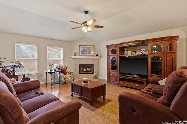 living room featuring vaulted ceiling, light hardwood / wood-style flooring, a tile fireplace, and ceiling fan