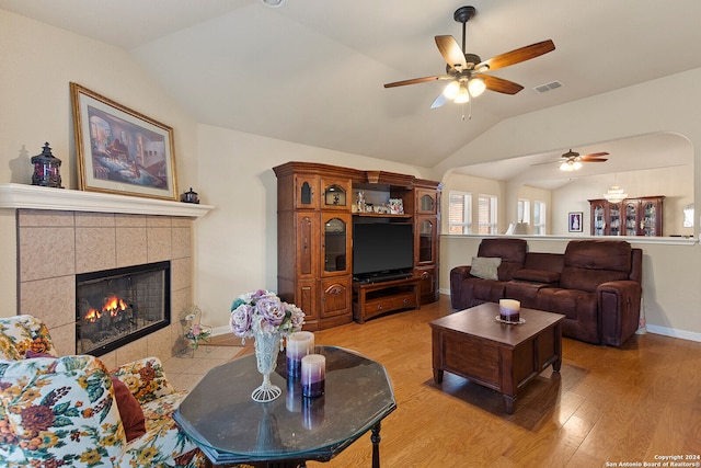 living room featuring light hardwood / wood-style flooring, a tile fireplace, vaulted ceiling, and ceiling fan