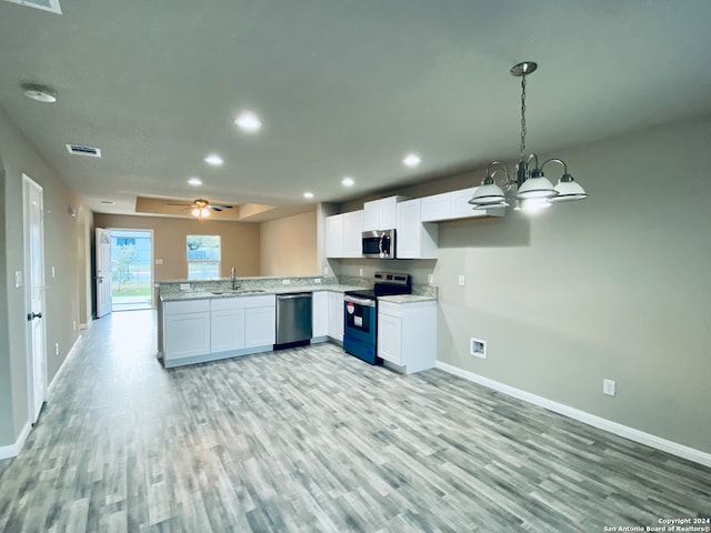 kitchen featuring kitchen peninsula, appliances with stainless steel finishes, white cabinetry, light wood-type flooring, and decorative light fixtures