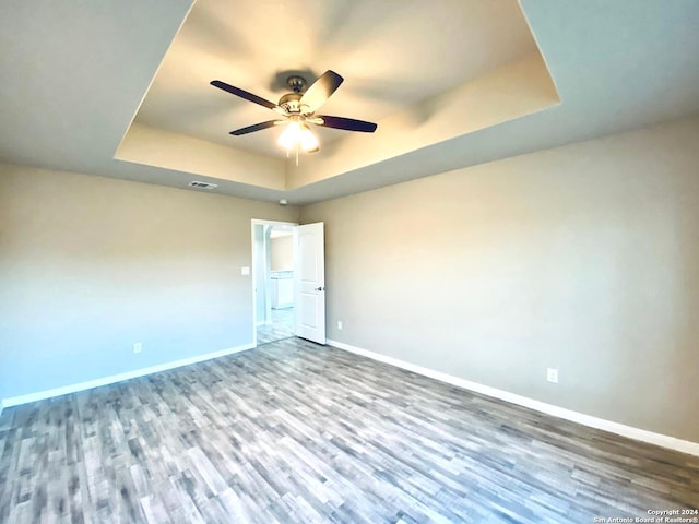 empty room featuring wood-type flooring, ceiling fan, and a tray ceiling