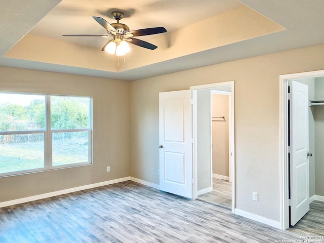 unfurnished bedroom with light hardwood / wood-style flooring, ceiling fan, a tray ceiling, a walk in closet, and a closet