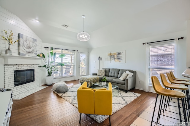 living room featuring lofted ceiling, hardwood / wood-style flooring, and a brick fireplace