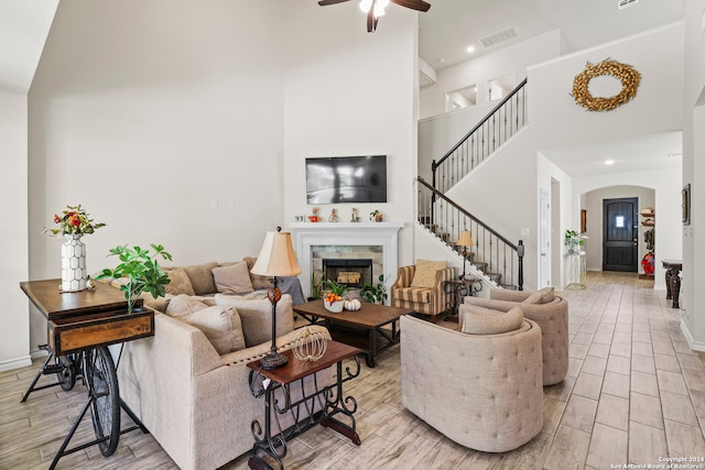 living room with light hardwood / wood-style floors, a fireplace, a high ceiling, and ceiling fan