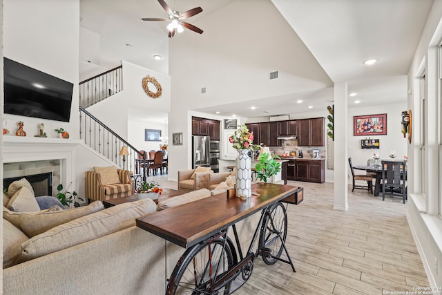 living room with a fireplace, high vaulted ceiling, light wood-type flooring, and ceiling fan