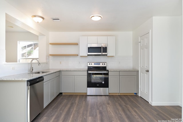 kitchen with stainless steel appliances, backsplash, sink, light stone countertops, and dark hardwood / wood-style flooring