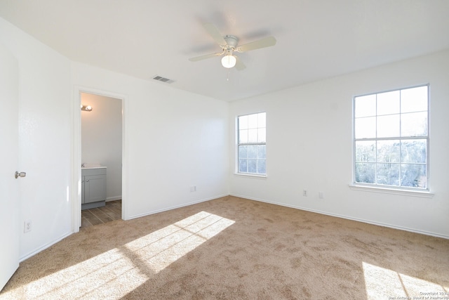 unfurnished bedroom featuring ensuite bathroom, light colored carpet, and ceiling fan