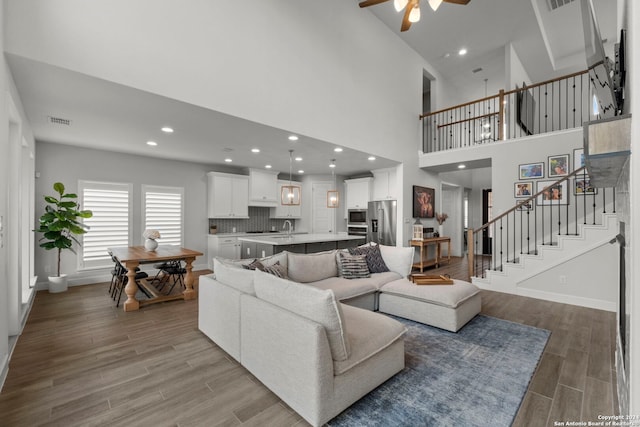 living room featuring a towering ceiling, light hardwood / wood-style flooring, sink, and ceiling fan