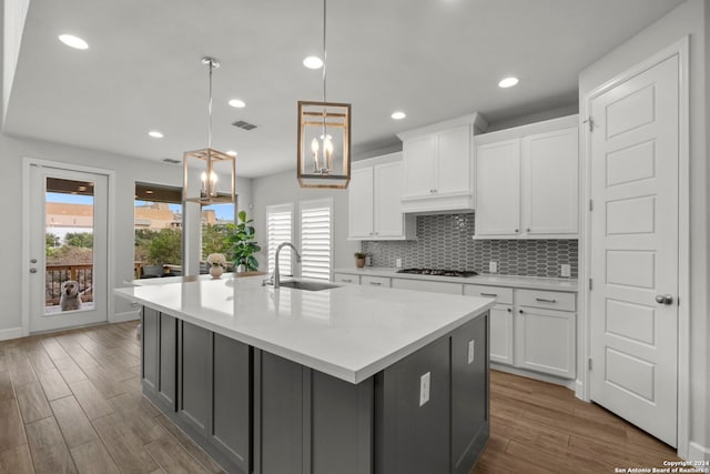 kitchen with a center island with sink, white cabinets, decorative light fixtures, and dark hardwood / wood-style flooring