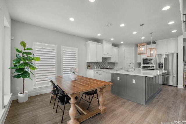 kitchen featuring stainless steel appliances, decorative light fixtures, a center island with sink, and white cabinets