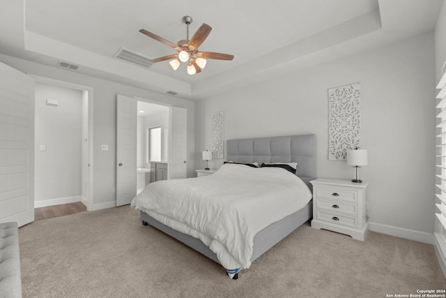 carpeted bedroom with ensuite bath, a raised ceiling, and ceiling fan