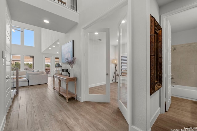 corridor with light hardwood / wood-style floors, french doors, and a high ceiling