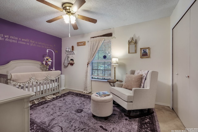 bedroom with light colored carpet, a textured ceiling, a crib, and ceiling fan