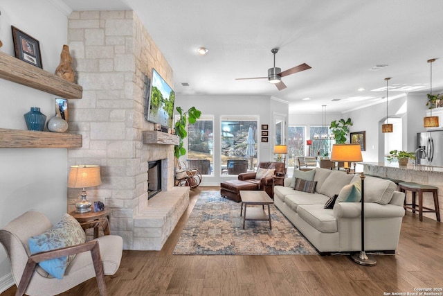 living room with hardwood / wood-style flooring, ornamental molding, ceiling fan, and a fireplace