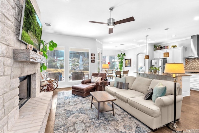 living room featuring crown molding, a fireplace, ceiling fan, and light wood-type flooring