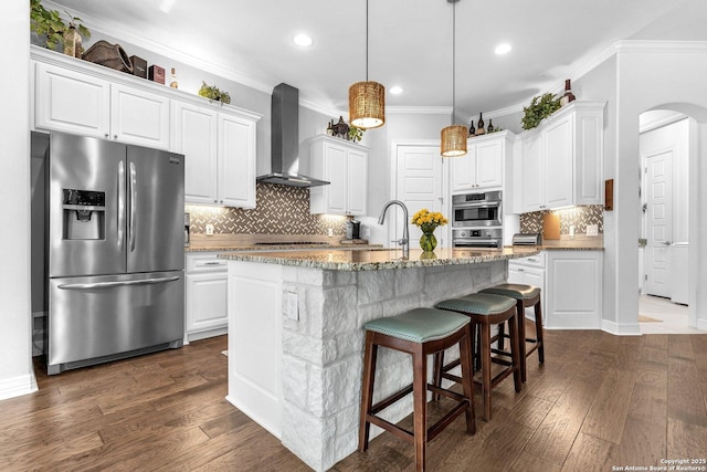 kitchen with wall chimney exhaust hood, sink, white cabinetry, appliances with stainless steel finishes, and a kitchen island with sink