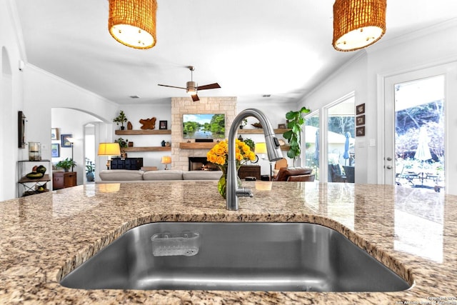 kitchen featuring stone counters, ornamental molding, sink, and a fireplace