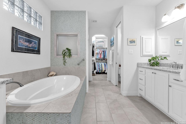 bathroom featuring a relaxing tiled tub, vanity, and tile patterned floors