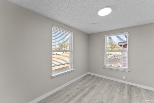 spare room with a textured ceiling, light wood-type flooring, and a wealth of natural light