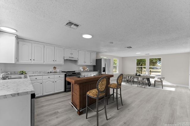 kitchen with black range with electric cooktop, sink, light wood-type flooring, a textured ceiling, and white cabinetry