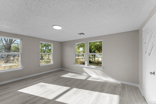 unfurnished room with light hardwood / wood-style flooring, a textured ceiling, and a healthy amount of sunlight