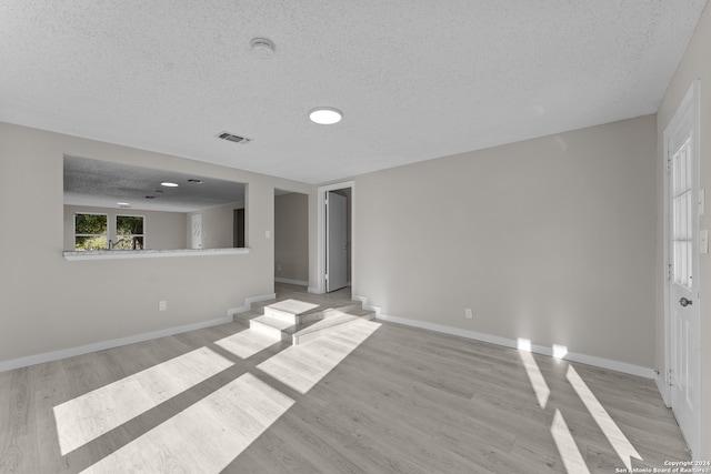 empty room with a textured ceiling and light hardwood / wood-style floors