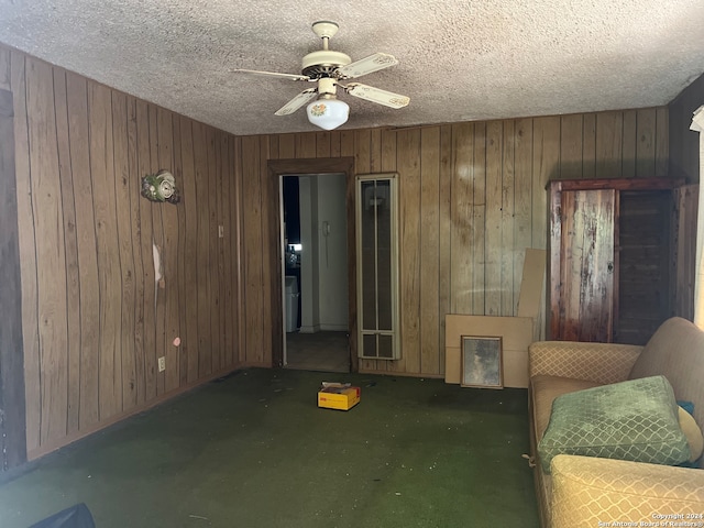 unfurnished living room with wood walls, a textured ceiling, dark carpet, and ceiling fan