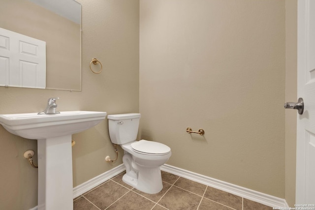 half bathroom featuring tile patterned floors, toilet, baseboards, and a sink