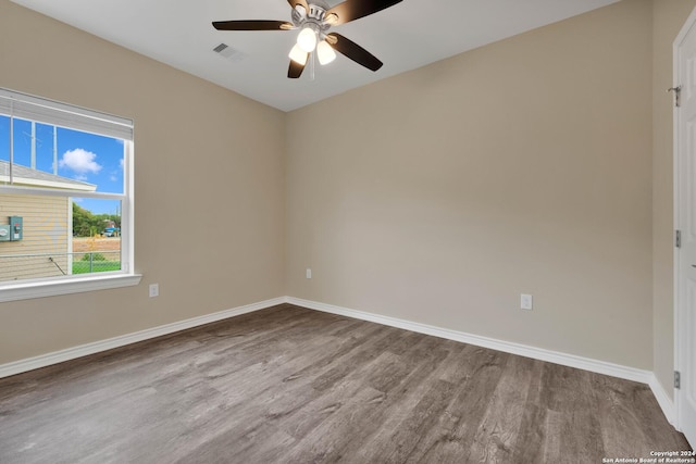 spare room with a ceiling fan, visible vents, wood finished floors, and baseboards