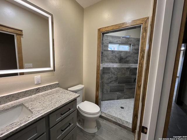 bathroom featuring toilet, a tile shower, and vanity