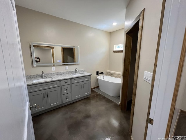 full bath featuring finished concrete floors, a freestanding tub, a sink, and double vanity