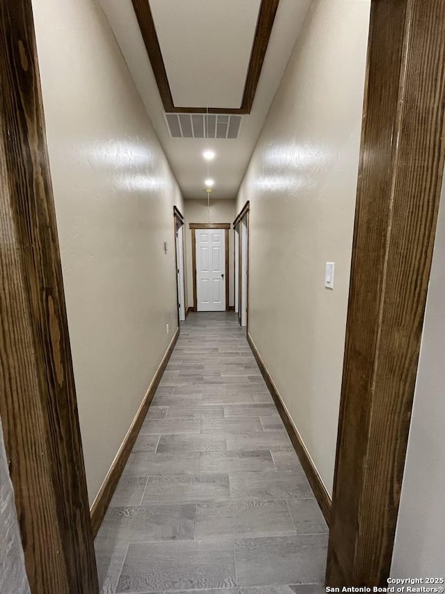 corridor featuring light wood finished floors, attic access, visible vents, and baseboards