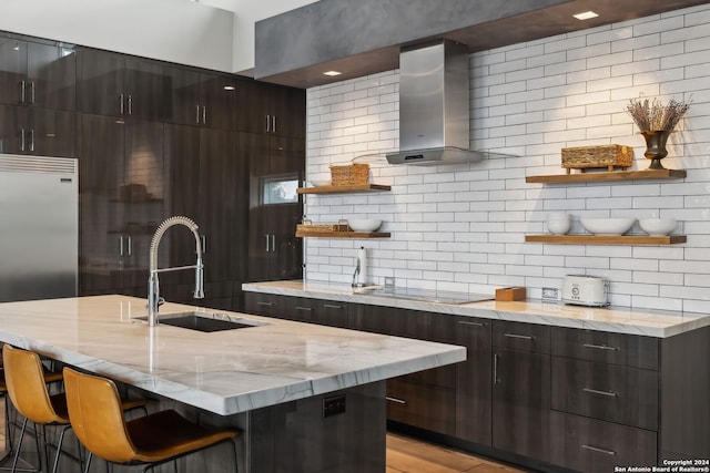 kitchen featuring decorative backsplash, a breakfast bar, wall chimney exhaust hood, sink, and black stovetop