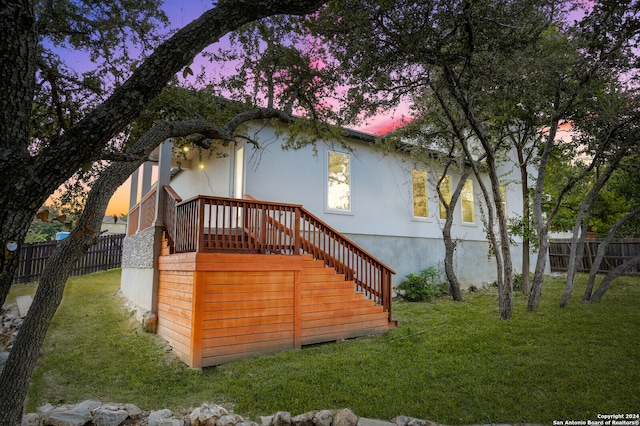 back house at dusk featuring a deck and a lawn