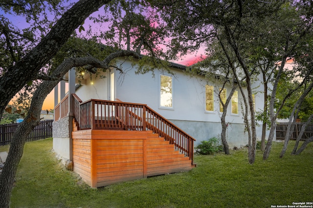 back house at dusk featuring a wooden deck and a lawn