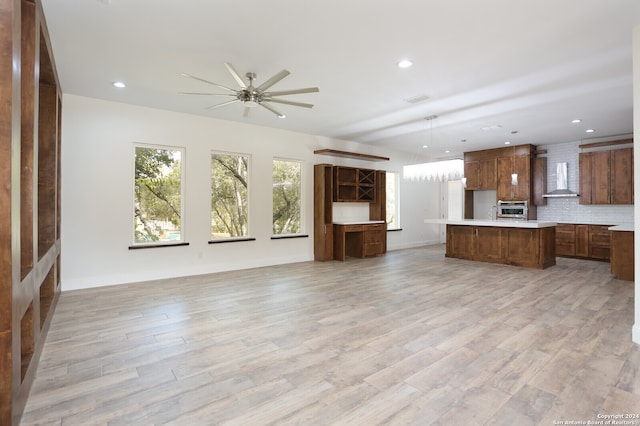 kitchen with tasteful backsplash, wall chimney range hood, light wood-type flooring, a kitchen island, and hanging light fixtures