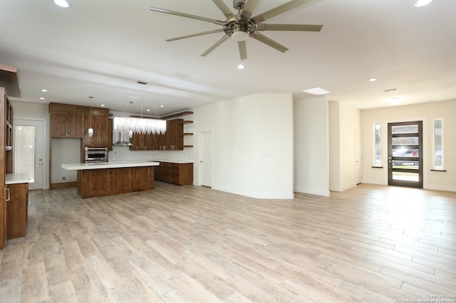 kitchen featuring oven, decorative backsplash, hanging light fixtures, a kitchen island, and light hardwood / wood-style flooring