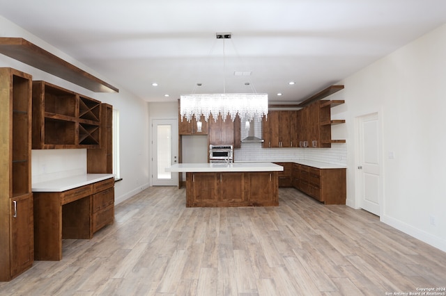 kitchen with oven, an island with sink, hanging light fixtures, light hardwood / wood-style flooring, and a chandelier