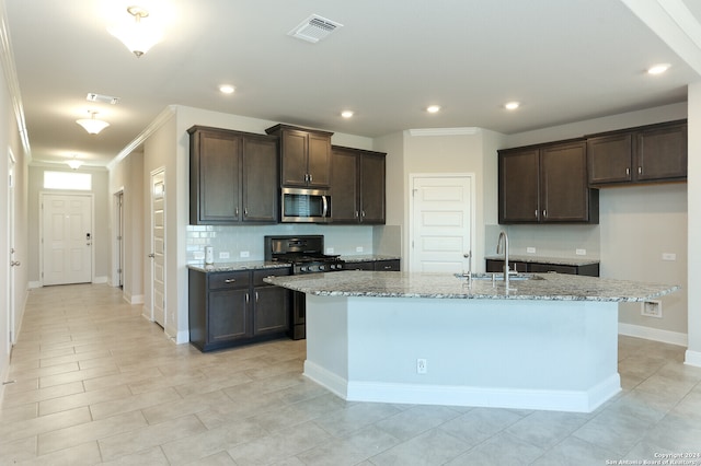 kitchen with light stone counters, crown molding, black gas stove, sink, and an island with sink