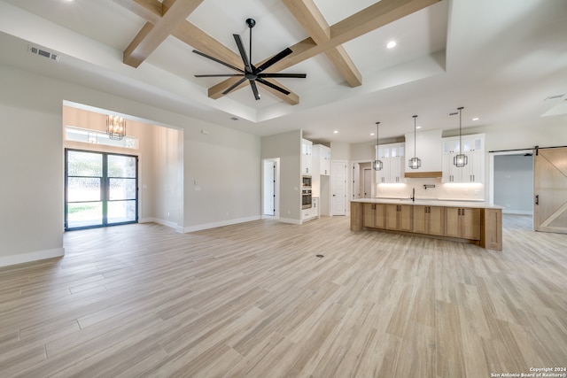 unfurnished living room with beam ceiling, a barn door, light hardwood / wood-style flooring, sink, and coffered ceiling