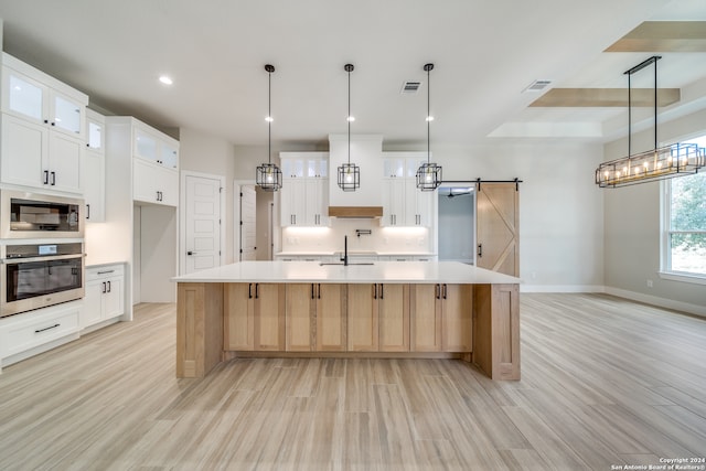 kitchen featuring a large island with sink, stainless steel oven, white cabinetry, and a barn door