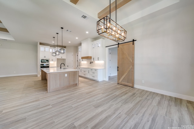 kitchen featuring a kitchen island with sink, hanging light fixtures, a barn door, white cabinets, and appliances with stainless steel finishes